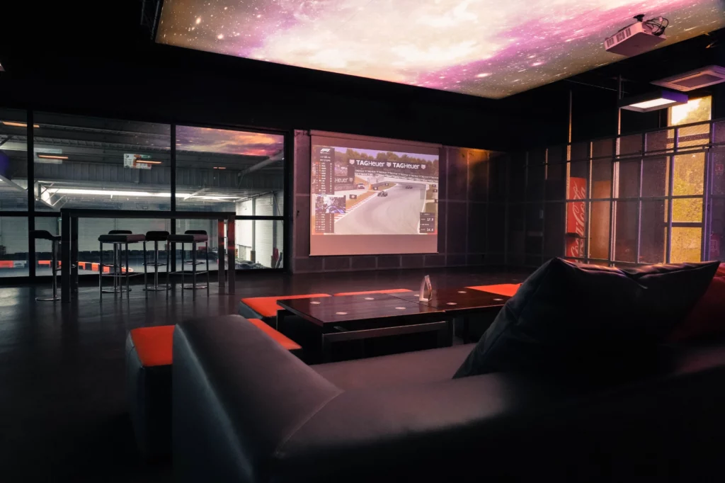 Salon panoramique de 400m² avec vue sur la piste, canapés et retransmissions sportives.